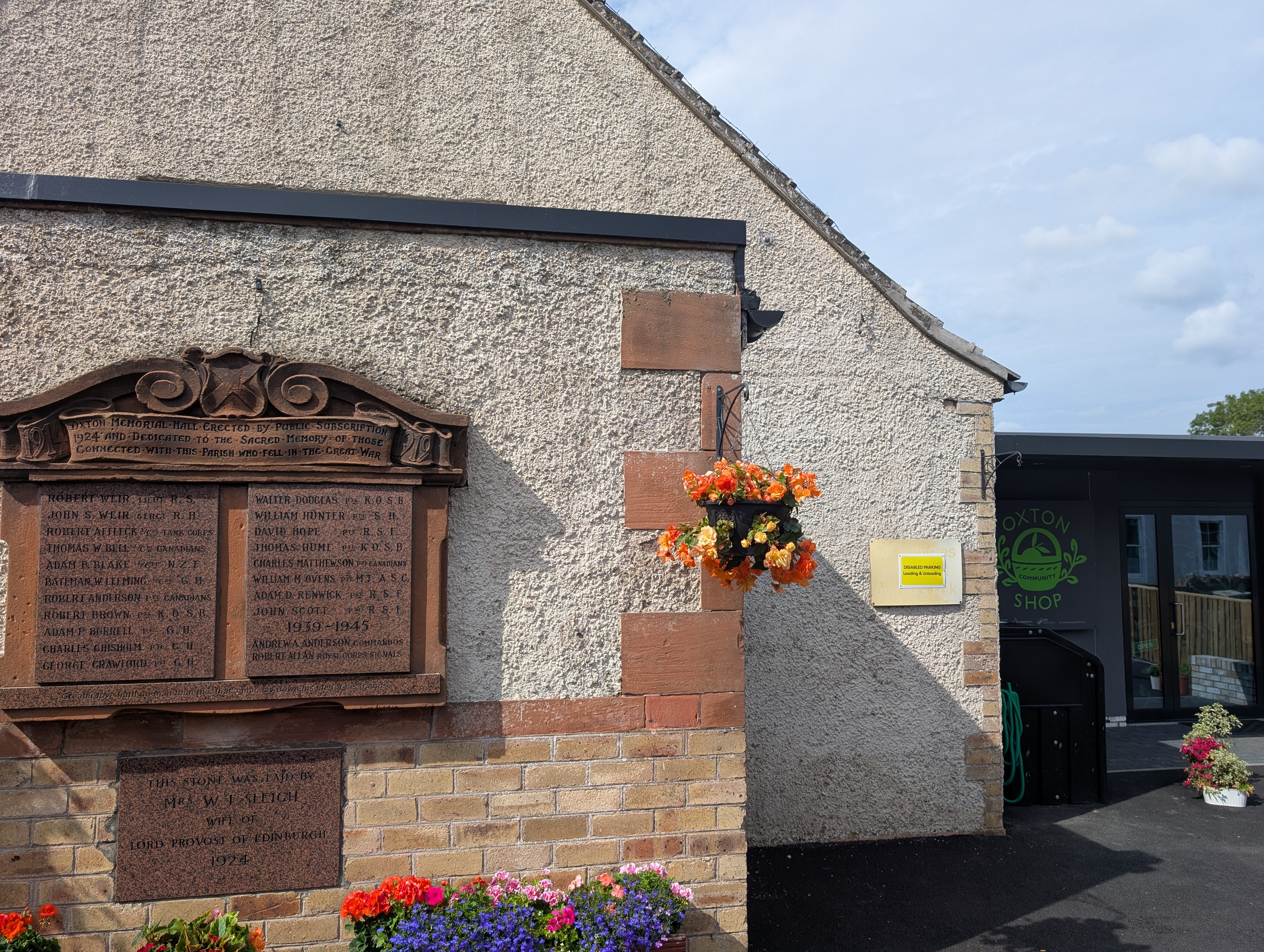 A photo of the Oxton War Memorial Hall, focussing on the plaque outside. The building is adorned with blooming flowers.